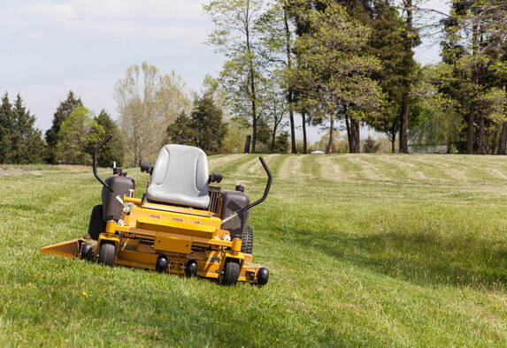 a ride-on lawn mowing machine sitting in a field of grass that is about to be mowed