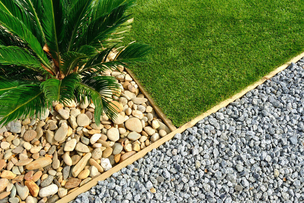 top angle photo of a landscaping garden bed separated by wood that has stones and fake grass